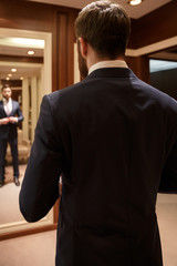 Vertical image of bearded man correcting his suit against mirror