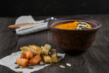 Pumpkin cream soup in a clay bowl with snack fried croutons bread,baked carrots on dark wooden  table