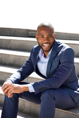 young african american business man sitting on steps outdoors and smiling