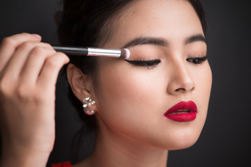Fototapeta premium Close up of hand of asian woman applying eyeshadow on female eyelid.