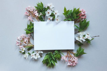 Spring background with paper sheet. Beautiful fresh flowers and leaves on gray background