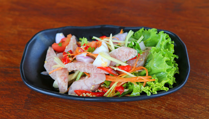 Thai sour pork sausage salad in black plate on wood table