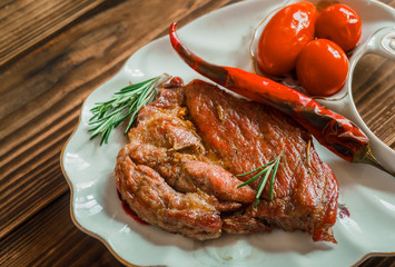 grilled meat with tomato and rosemary on the dish with wooden background