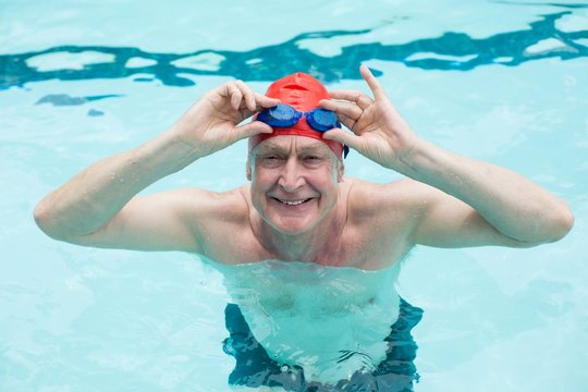 Happy senior man holding goggles in swimming pool