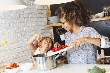 Beautiful African American woman and her daughter cooking in the kitchen 