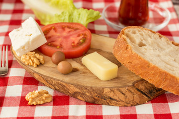 Small Turkish Breakfast plate, white cheese, kashkaval cheese, tomato, slice of bread, green olives, lettuce, walnuts and glass of tea on plaid table cloth