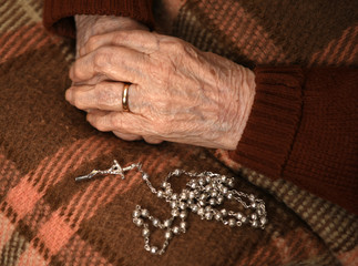 Obraz premium Close up of old woman praying with silver rosary with cross