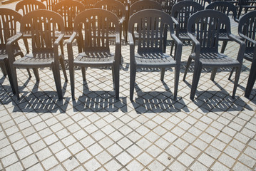 Many empty plastic black chairs rests on the floor in outdoor event.