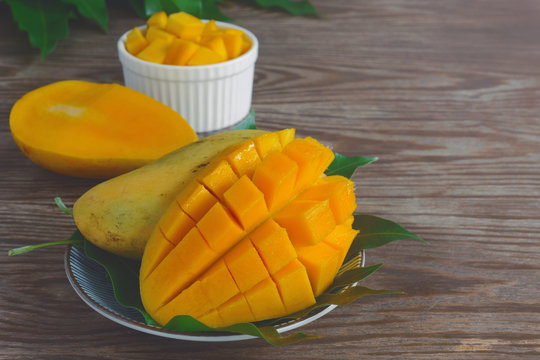sliced of ripe yellow mangoes with fruit and green mango leaf served with white bowl on wood table in the background.