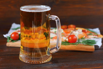 Mug of light beer and pizza with smoked meat are on dark wooden background.