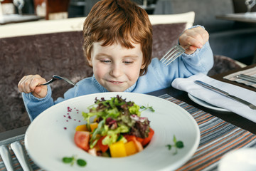 Red haired boy with forks eating salad