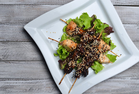 Yakitori with sesame seeds on a plate. Fried chicken meat and chicken liver on sticks on a wooden table. Top view.
