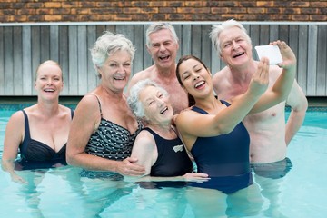 Female trainer taking selfie with senior swimmers in pool