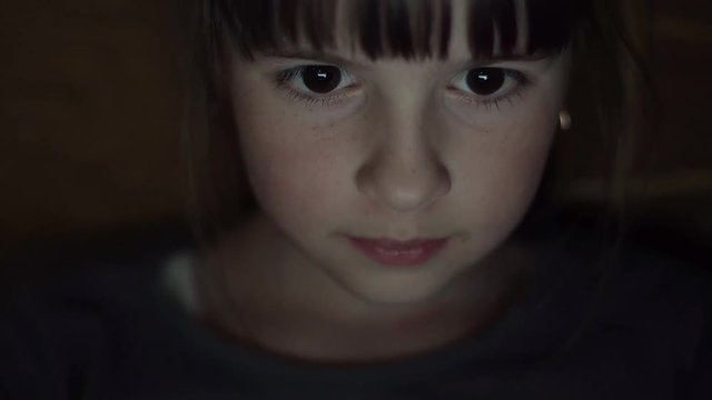 Night shot of kid's girl face browsing tablet pc with light reflection on it