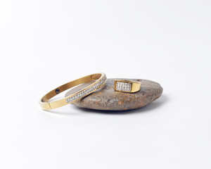 wedding ring and gold bracelet isolated on stone on a white background.
