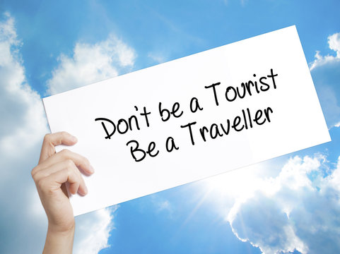 Don't be a Tourist Be a Traveller  Sign on white paper. Man Hand Holding Paper with text. Isolated on sky background