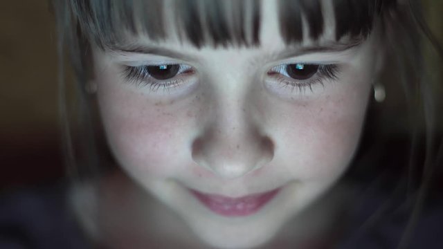 Night shot of kid's girl face browsing tablet pc with light reflection on it