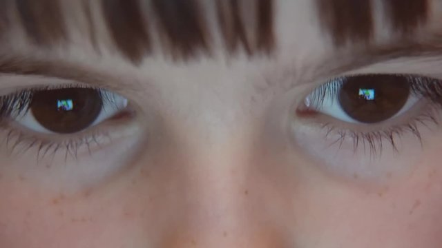 Closeup night shot of kid's girl eyes browsing tablet pc with light reflection on it