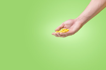 Yellow pills in hand on green background.