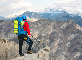 Young mountaineer standing with backpack on top of a mountain and enjoying the view