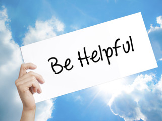 Be Helpful Sign on white paper. Man Hand Holding Paper with text. Isolated on sky background.