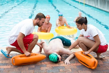 Male and female lifeguards helping unconscious man 