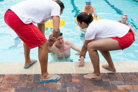 Lifeguards helping unconscious senior man in swimming pool