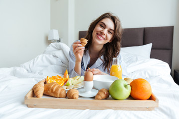 Obraz na płótnie Canvas Portrait of a pretty happy woman having breakfast in bed