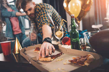 man eating stale pizza in messy room after party