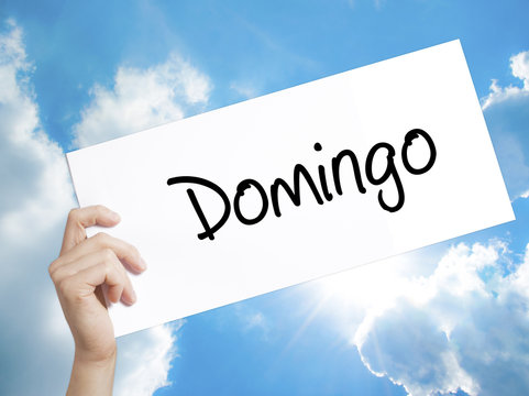 Domingo  (Sunday in Spanish/Portuguese) Sign on white paper. Man Hand Holding Paper with text. Isolated on sky background