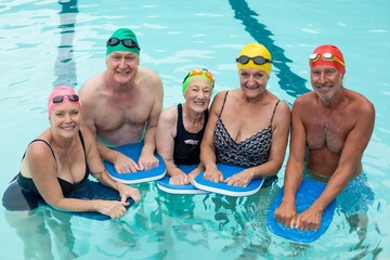 Senior swimmers posing with kickboards in pool