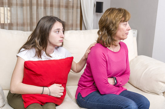 Teen girl is sad because her mother is angry while sitting on sofa at home.