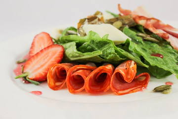 Mix of hot sausages with bacon on a cushion of lettuce leaves, in a duet with parmesan and strawberries, garnished with pumpkin seeds, dressed with raspberry sauce