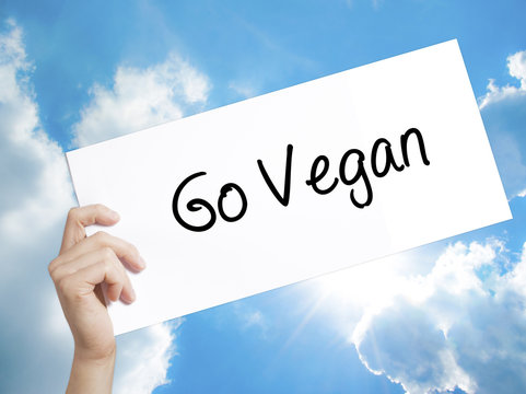 Go Vegan Sign on white paper. Man Hand Holding Paper with text. Isolated on sky background
