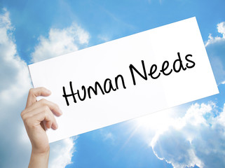 Human Needs Sign on white paper. Man Hand Holding Paper with text. Isolated on sky background.