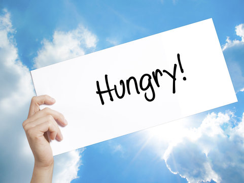 Hungry! Sign on white paper. Man Hand Holding Paper with text. Isolated on sky background