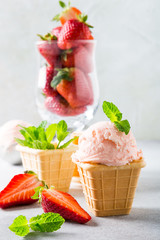 Waffle cup with homemade strawberry ice cream and mint leaves, glass full of strawberries on gray stone background. Healthy summer food.