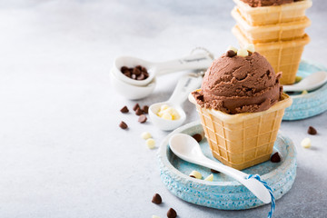Waffle cups with chocolate ice cream, milk and white chocolate granules in measuring spoons on gray stone background. Healthy summer food concept with copy space.
