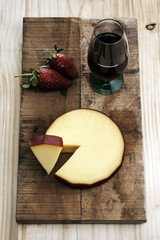 Smoked cheese portion, with whole cheese and wine on rustic background.