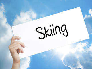 Skiing Sign on white paper. Man Hand Holding Paper with text. Isolated on sky background