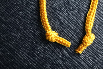 Gold color rope cable with simple knot close up photo hanging down in front of the black color...