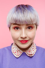 Fashion close-up portrait of smling beautiful dollish girl with short light violet hair wearing lilac sweater over pink background.