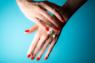 Hands of a young girl with red nails and drops of cream close-up on a blue background