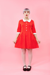 Picture of beautiful dollish girl with short light violet hair wearing red dress over pink background.
