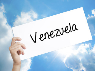 Venezuela Sign on white paper. Man Hand Holding Paper with text. Isolated on sky background