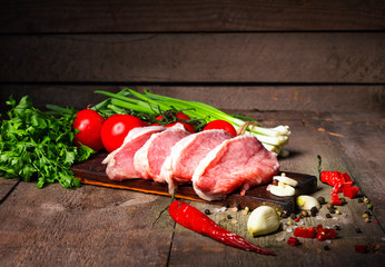 Raw juicy meat steaks ready for roasting on a black chalk board. Fillet with cherry tomatoes, hot pepper and herbs. Space for text