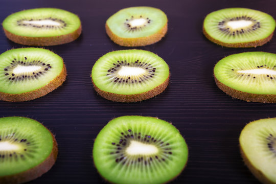 Colorful fruit pattern of fresh kiwi slices on dark wooden background.
