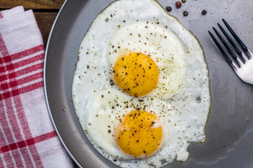 Two fried eggs in pan with peppercorns