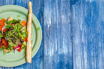 Salad of tomatoes, onions, bell pepper, cheese and herbs, bread stick on a green plate, stand