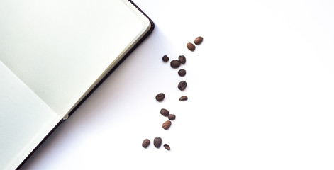 Coffee beans and opened notepad on white background. Top view with copy space